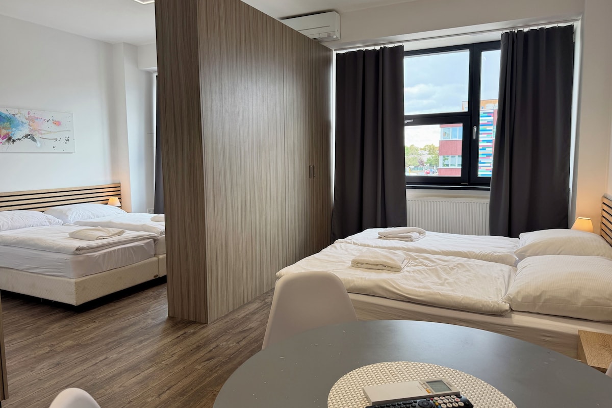 Ein Hotelzimmer mit zwei Betten, einem Esstisch und Blick auf die Stadt durch ein Fenster.