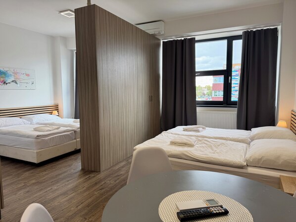 A hotel room with two beds, a dining table, and a view of the city through a window.