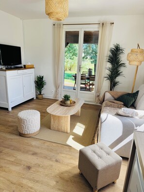 A modern living room with a flat-screen TV, a sofa, a coffee table, and a dining area with a table and chairs.