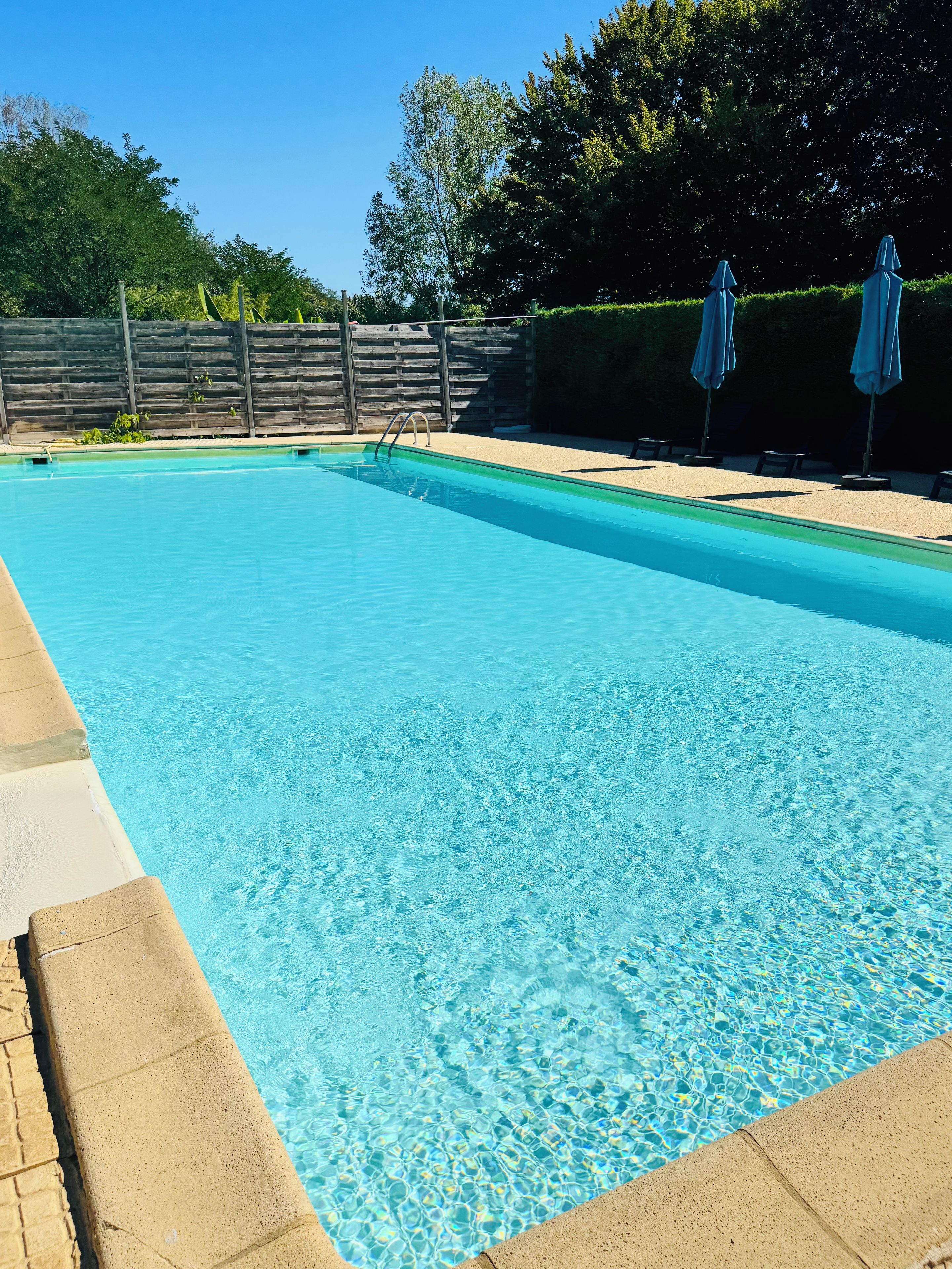 Une piscine rectangulaire à l’eau d’un bleu cristallin, entourée d’une zone sablonneuse agrémentée de chaises longues et de parasols.