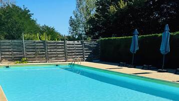 Une piscine rectangulaire à l’eau d’un bleu cristallin, entourée d’une zone sablonneuse agrémentée de chaises longues et de parasols.