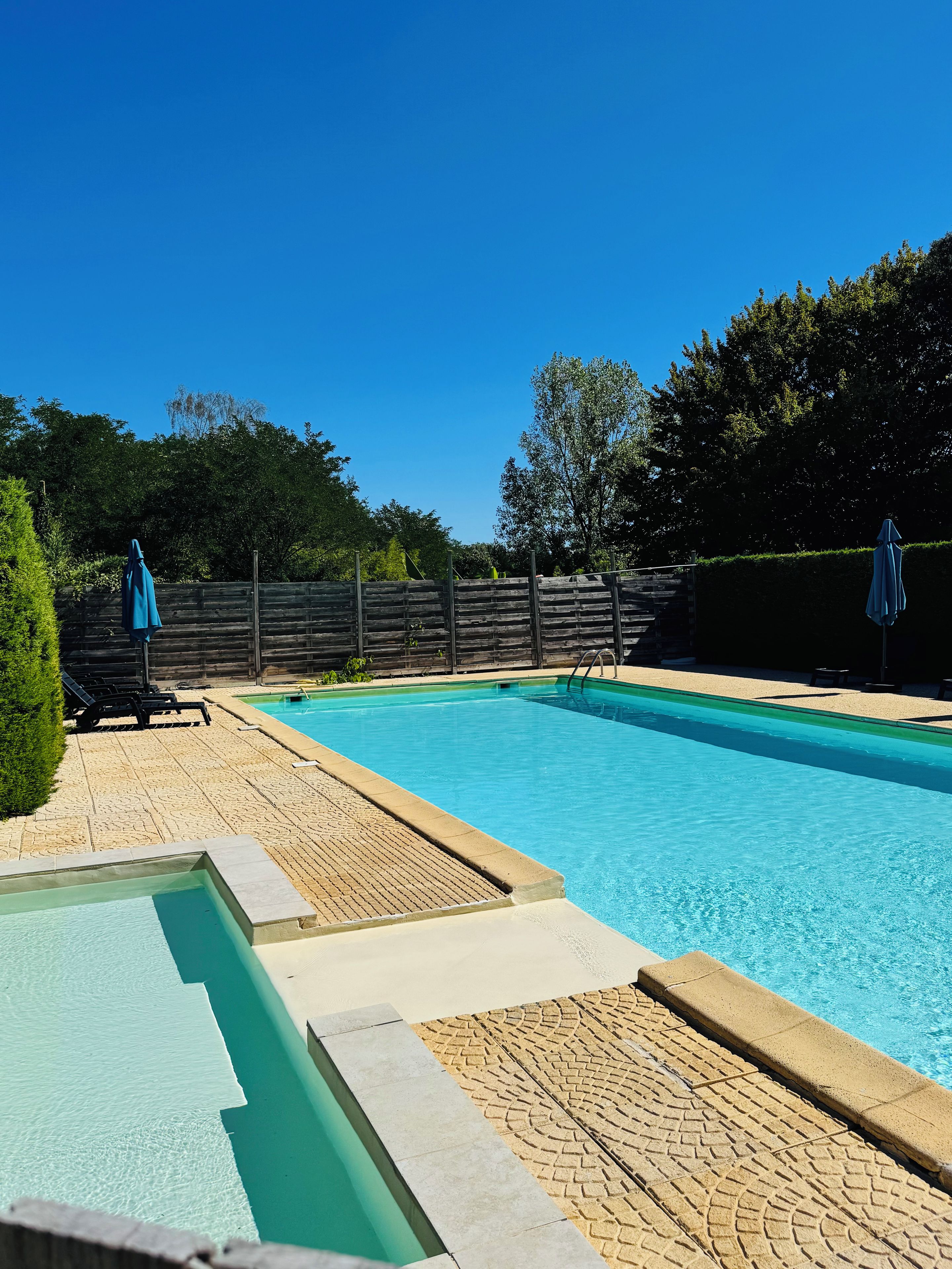Ein rechteckiger Pool mit einer gefliesten Liegefläche und einem angrenzenden, kleineren Pool.