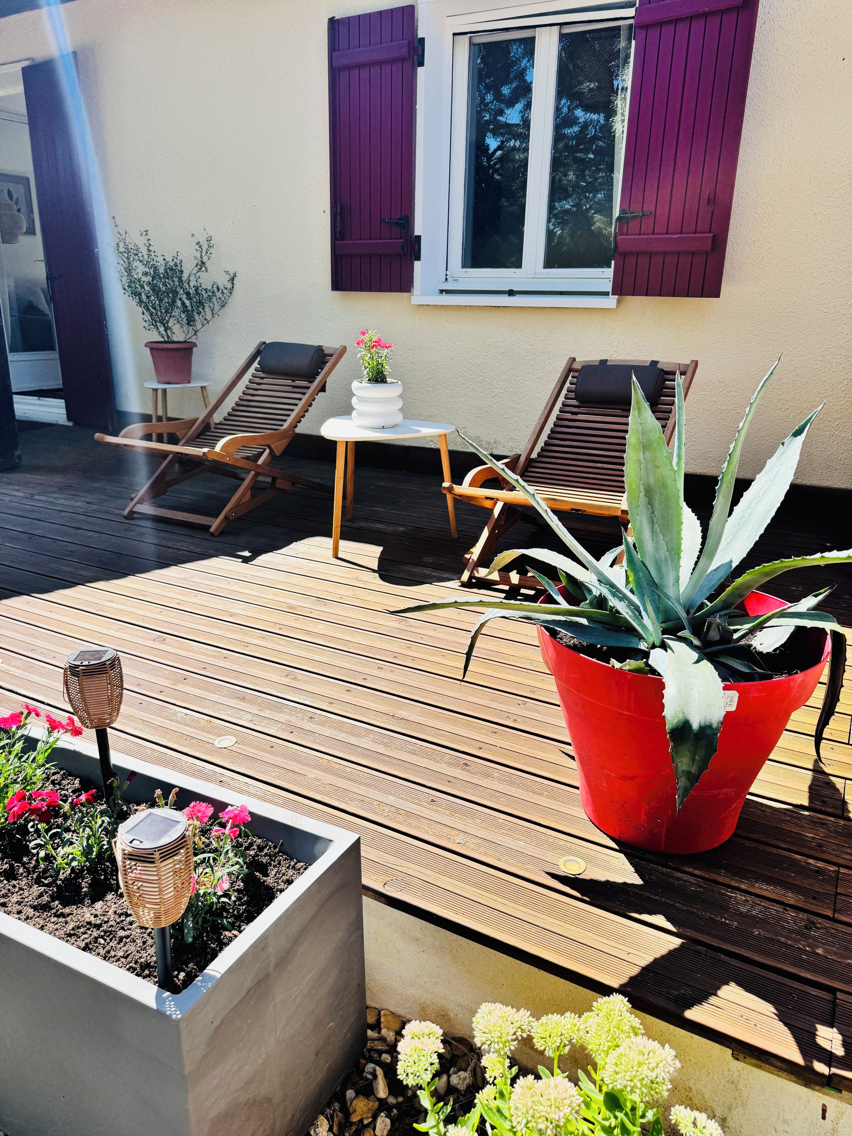 Een houten terras met twee lounge stoelen, een bijzettafeltje en plantenpotten.