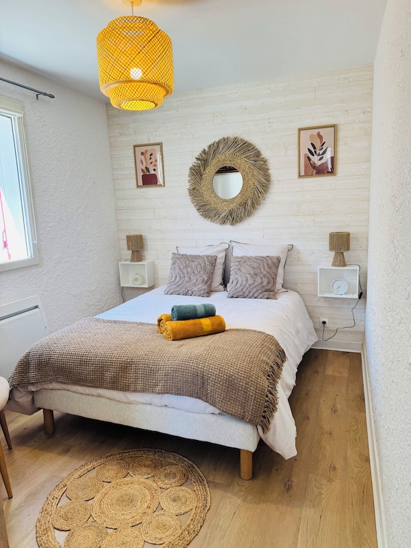 A bedroom with a bed, bedside tables, a wall-mounted mirror, and a woven rug.