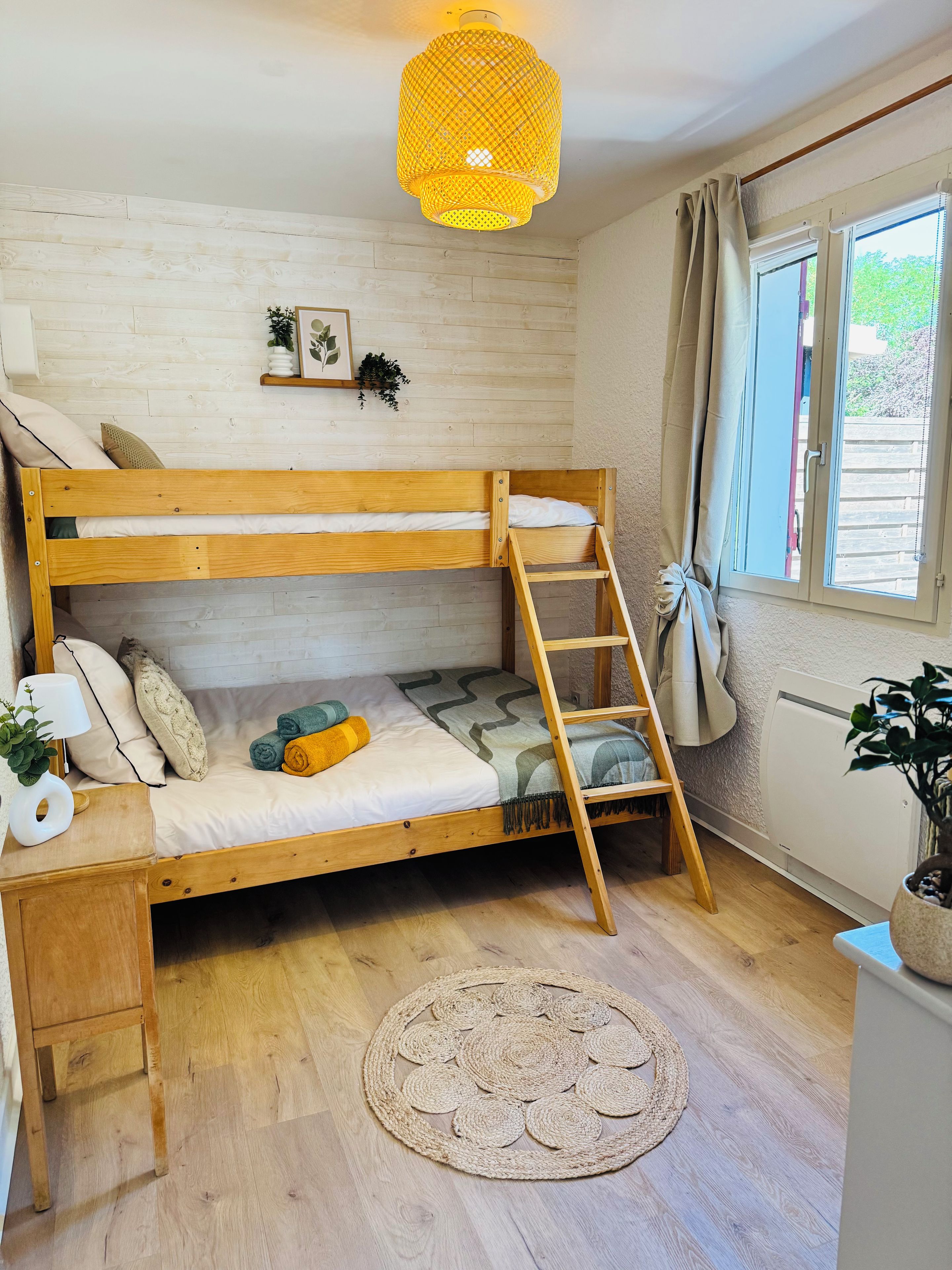 Un lit superposé avec une échelle, un petit bureau, un tapis tissé et un luminaire suspendu.