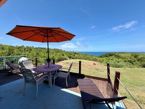 Eine Terrasse mit Gartenmöbeln, darunter ein Tisch und Stühle, und ein großer Sonnenschirm, der Schatten spendet.