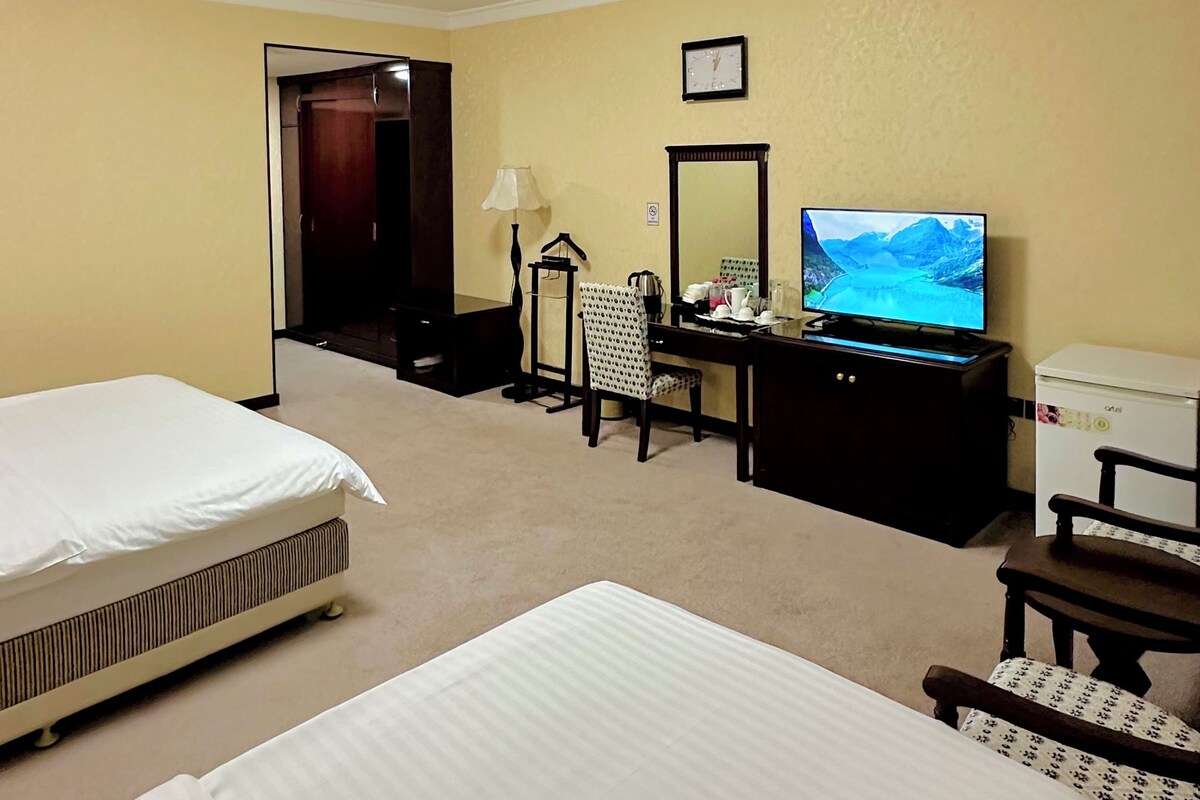 A hotel room with two beds, a desk with a computer, a TV, and a wardrobe.