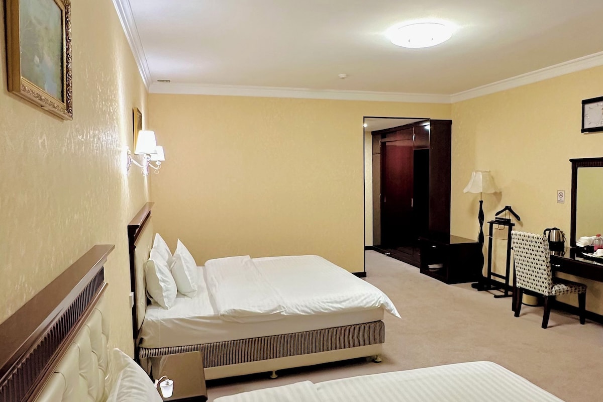 A hotel room with two beds, a desk, a chair, and a wardrobe.