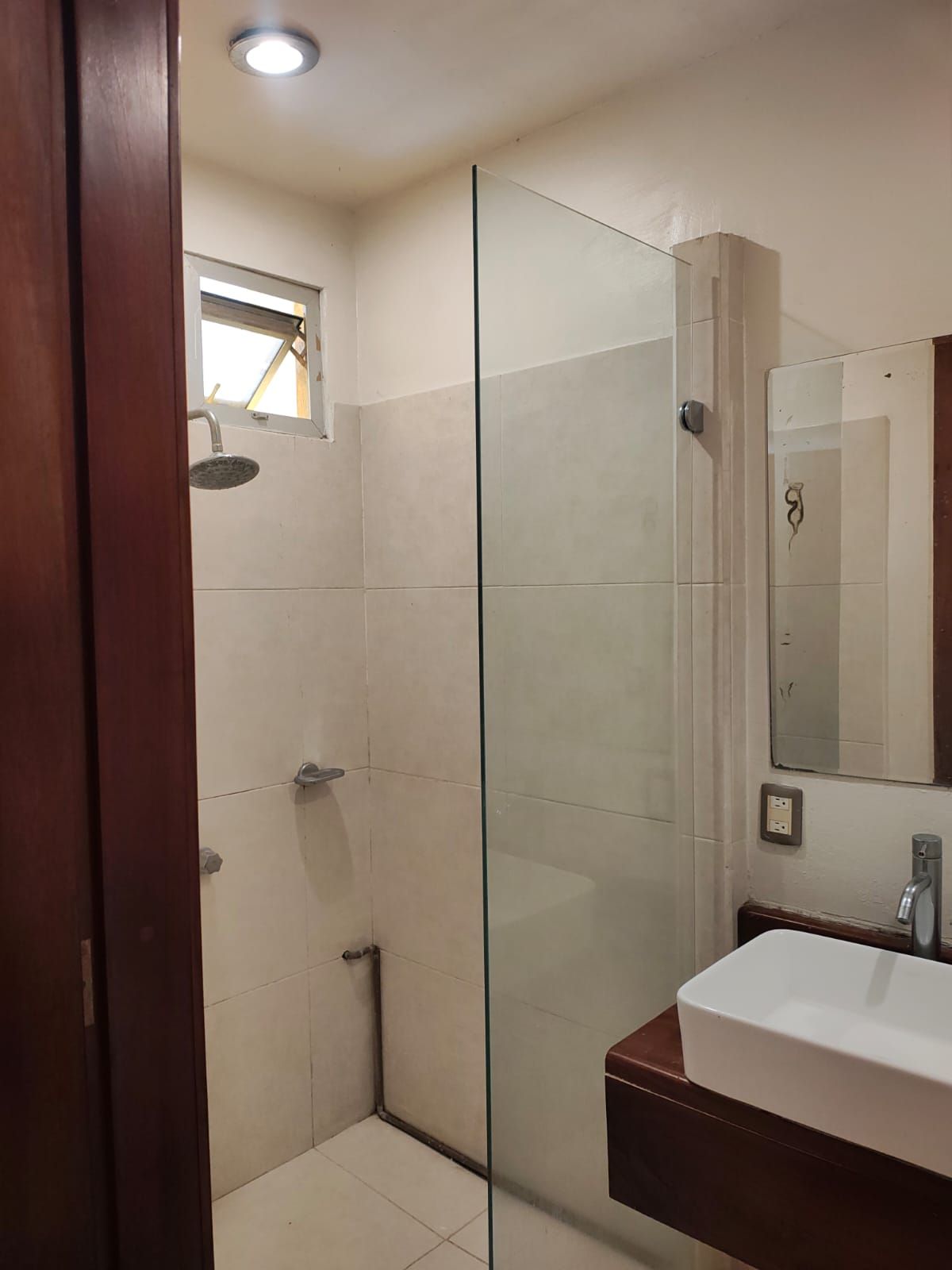 Un baño con cabina de ducha de vidrio, un lavabo blanco y un espejo.