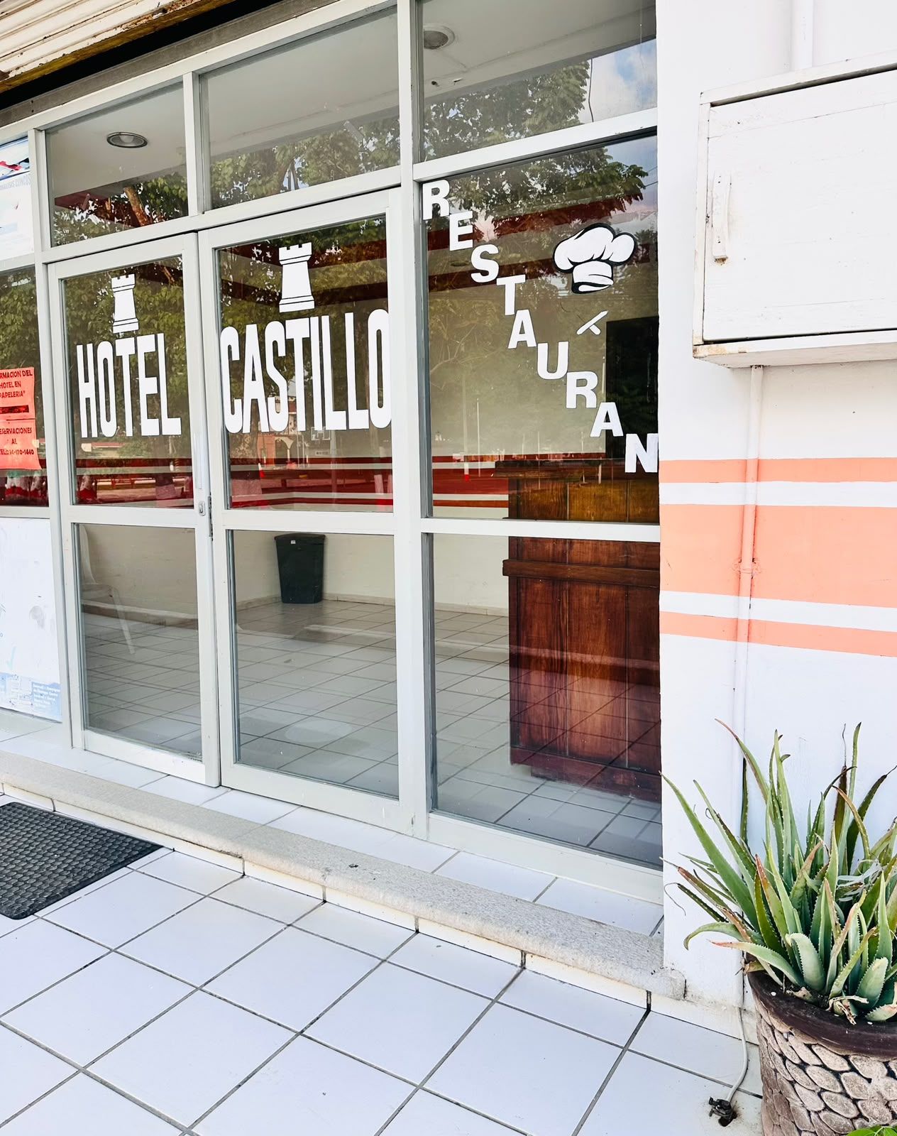 Ein Hotel Eingang mit der Beschilderung 'HOTEL CASTILLO' und einem Schild für 'RESTAURANT', das durch das Fenster sichtbar ist.