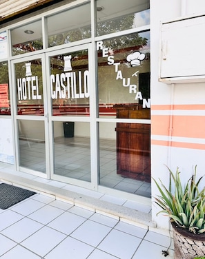 Een hotelentree met 'HOTEL CASTILLO' aanduiding en een 'RESTAURANT' bord zichtbaar door het raam.