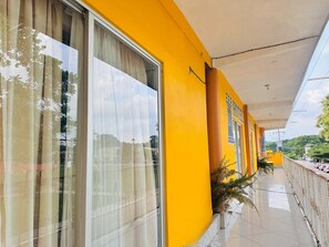 Un pasillo de hotel con ventanas amplias, piso de baldosas y una pared exterior amarilla.