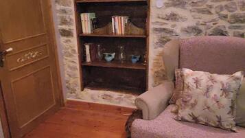 A room with a wooden door, a bookshelf, a patterned armchair, and a stone wall.