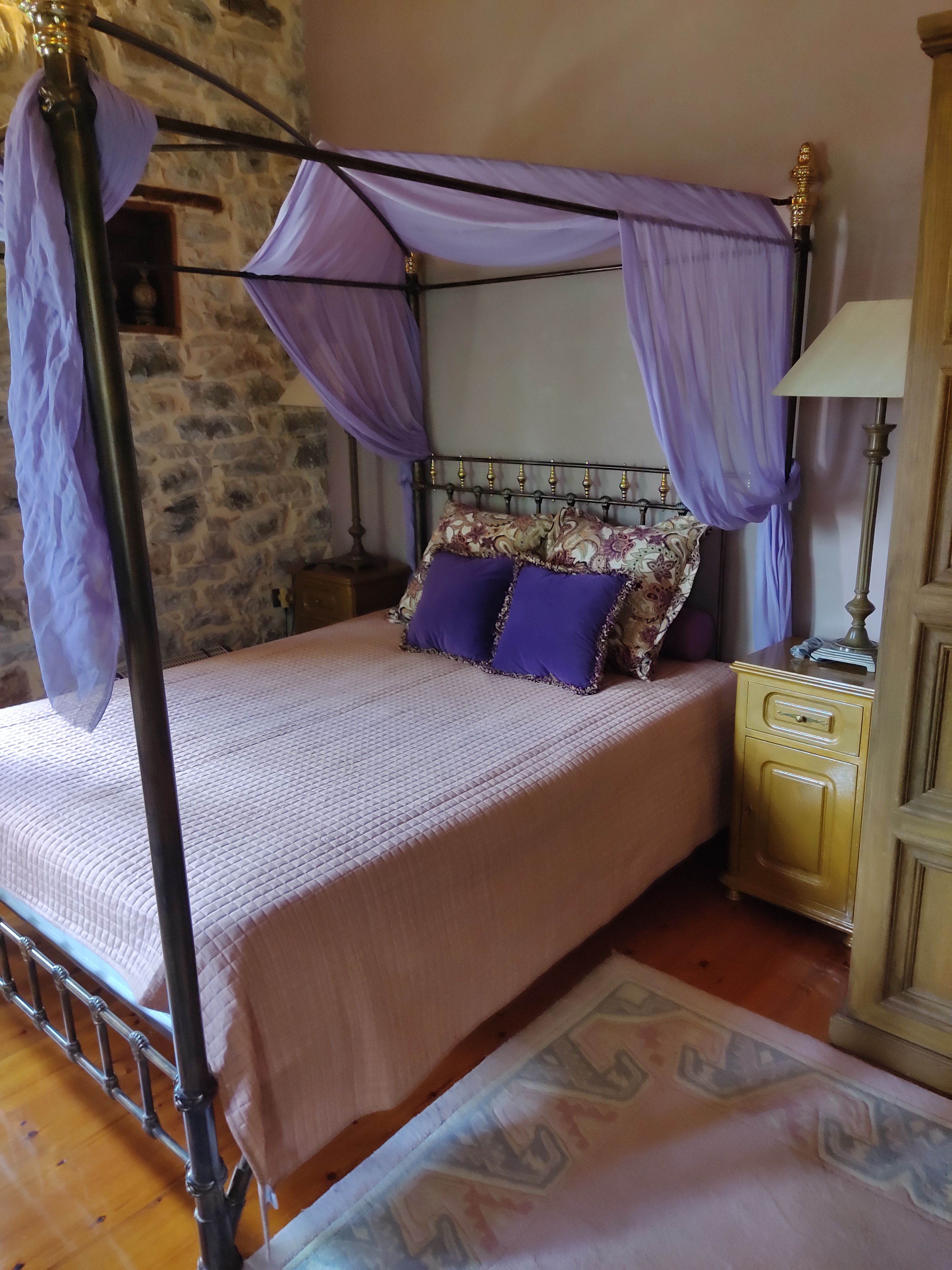 A bed with a canopy, a nightstand, a lamp, and a patterned rug.