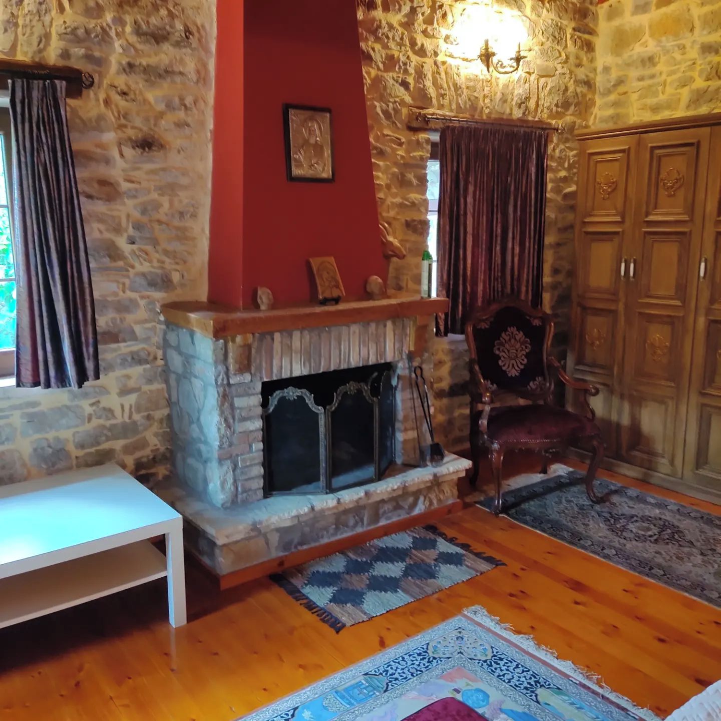 A stone-walled room with a fireplace, a wooden chair, and a patterned rug.