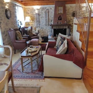 A cozy living room with a stone wall, a fireplace, and a staircase.