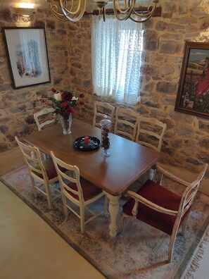 A dining area with a stone wall, a chandelier, and a table set for four. - Ενοικιαζόμενη βίλλα μέχρι 9 άτομα μια εμπειρία διαμονής στα Καλάβρυτα για δράση (Kleitoria)