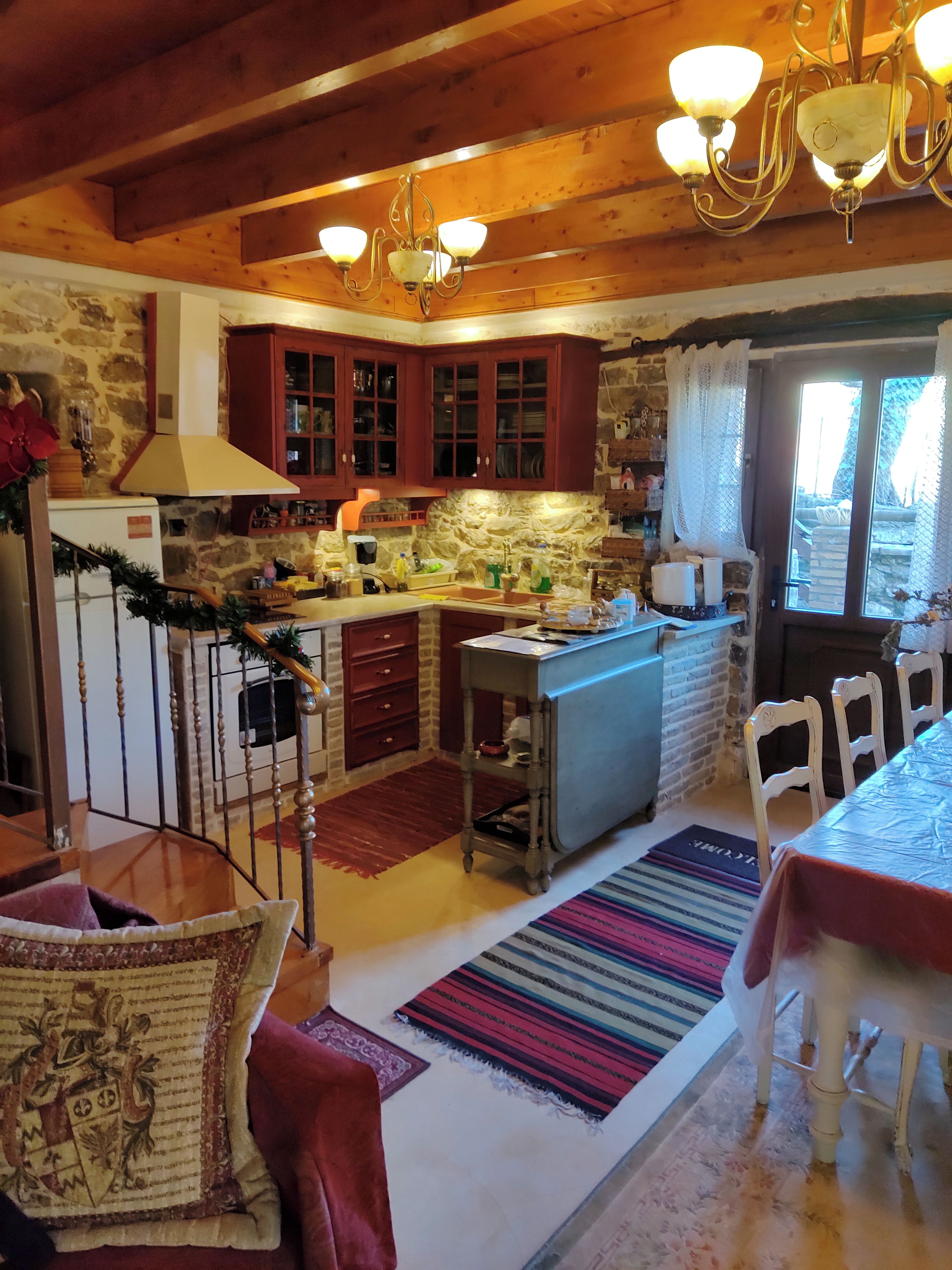 Una cocina rústica con vigas de madera, paredes de piedra y una zona de comedor con una mesa y sillas.