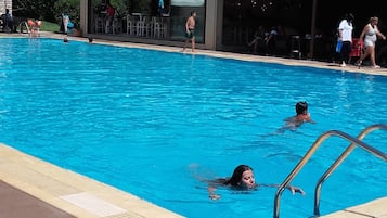 A swimming pool with clear blue water, surrounded by a covered area with a tiled roof.