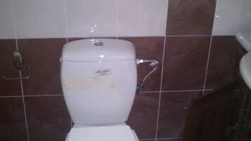 Un inodoro blanco estándar en un baño con paredes cubiertas de azulejos marrón oscuro y blanco.