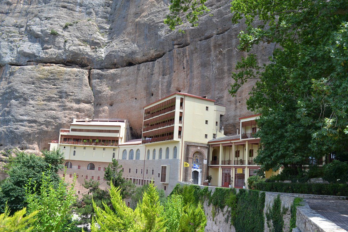 A multi-story building with balconies, set against a large rock face.