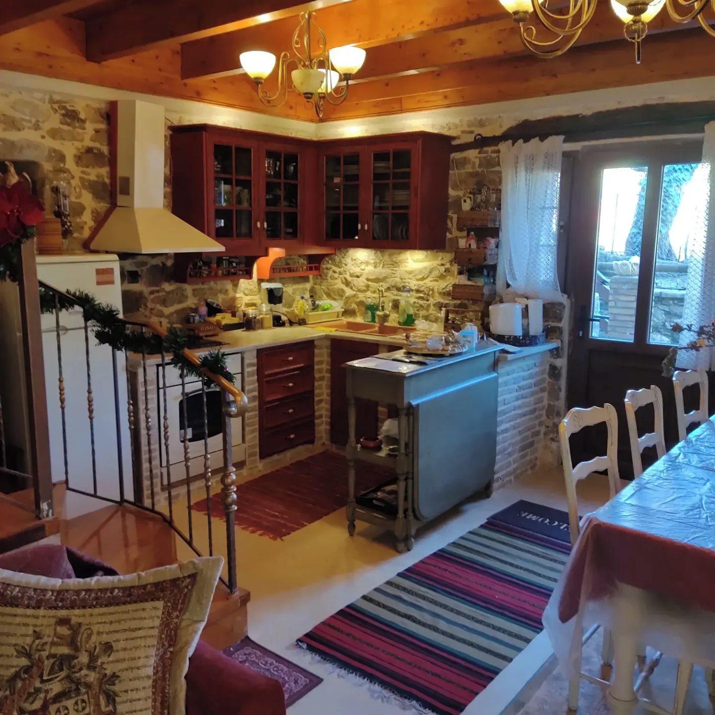 Una cocina con armarios de madera, pared de piedra y ventana con cortinas.
