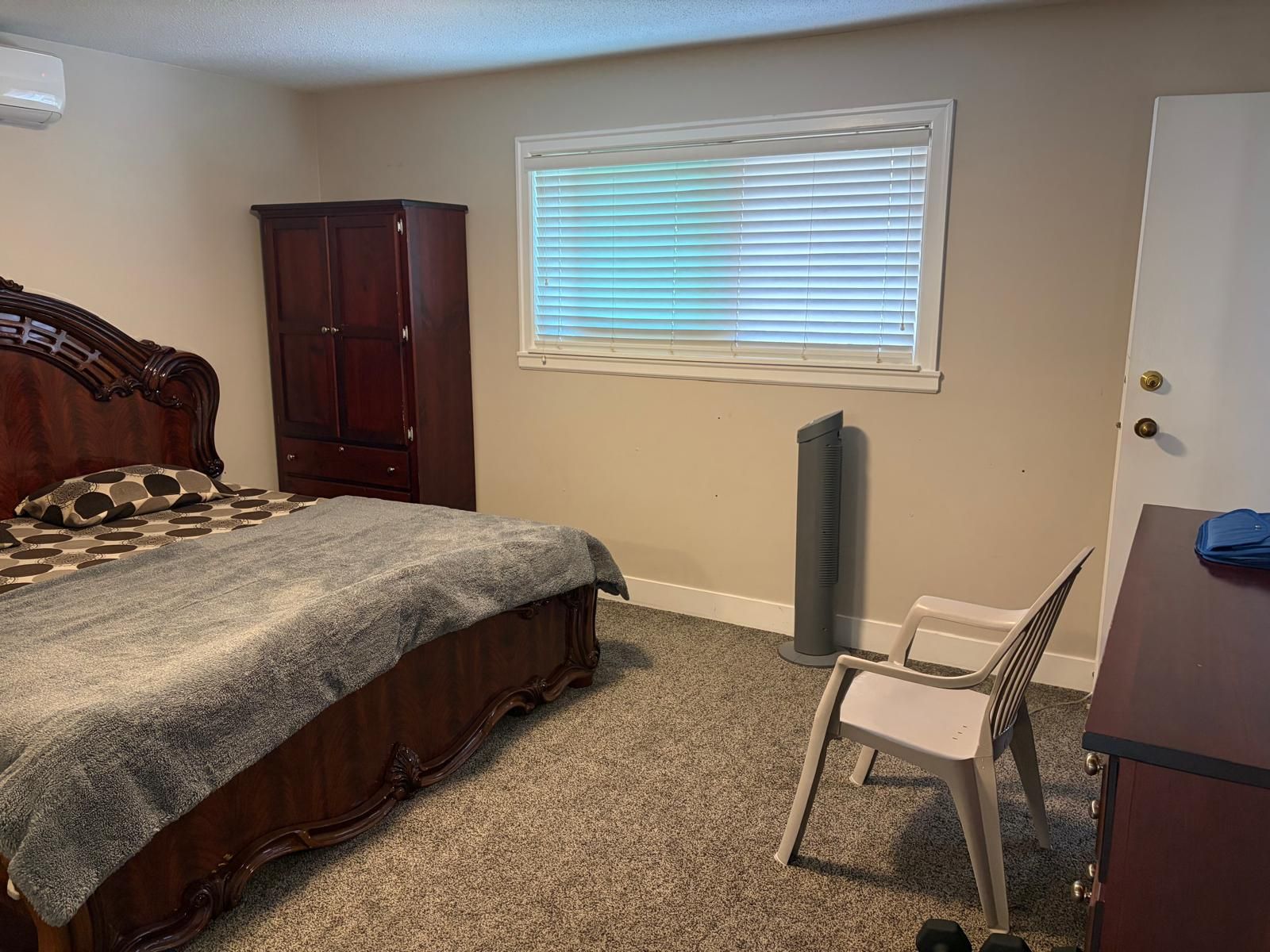 A bedroom with a bed, a wardrobe, a radiator, a window with blinds, and a chair.