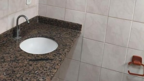 Un baño con lavamanos de granito, un espejo y dos ganchos para toallas.