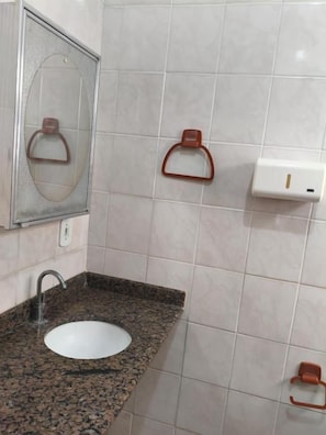 Un baño con lavamanos de granito, un espejo y dos ganchos para toallas.