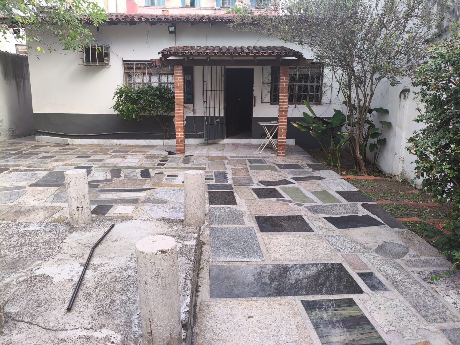 Pátio com piso de azulejos, um pilar de tijolos e uma porta que dá para uma entrada coberta.
