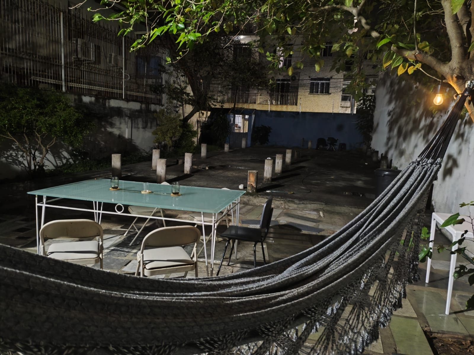 Un espacio al aire libre con mesa y sillas, una hamaca y una planta en maceta.