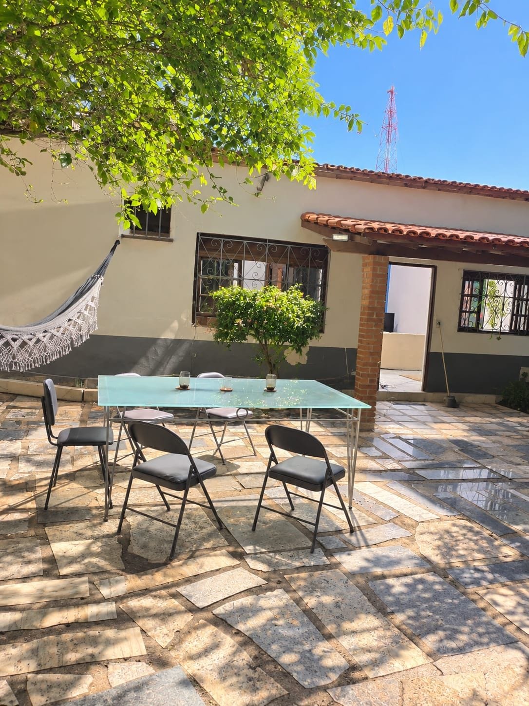 Un patio al aire libre con una mesa, sillas, una hamaca y una planta en maceta.