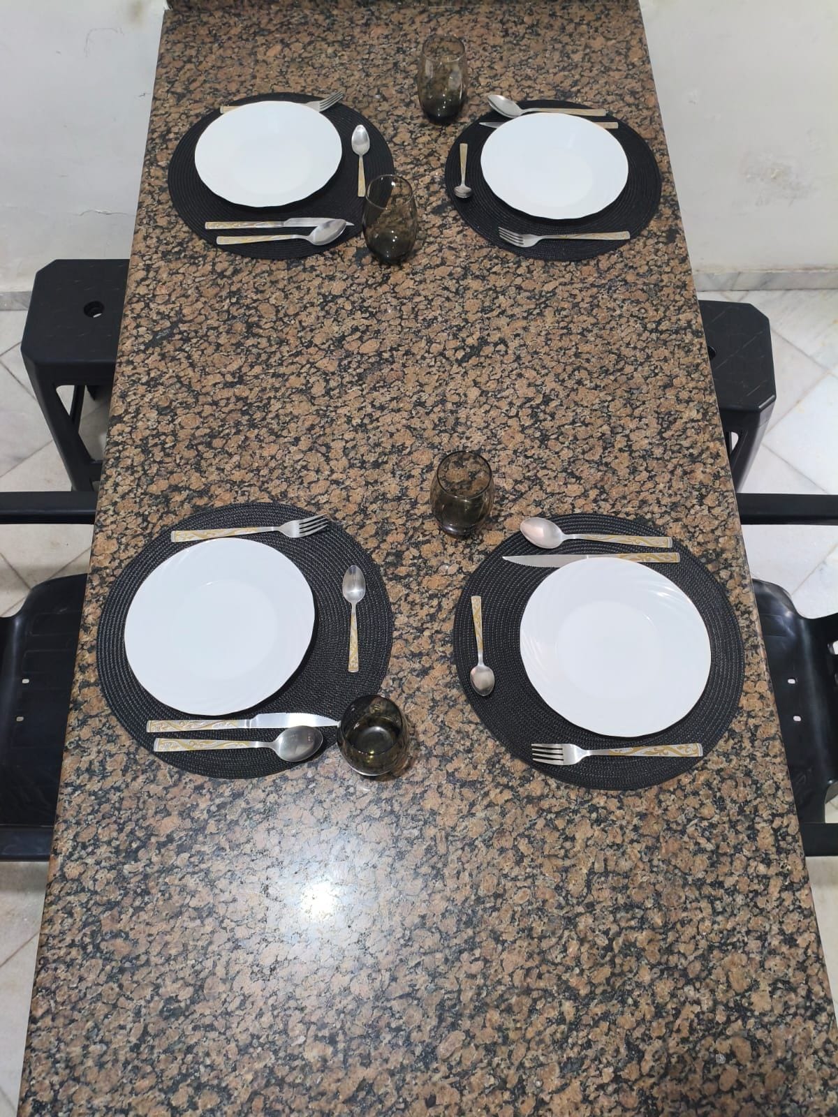 Une table rectangulaire en granit, sur laquelle sont disposés quatre couverts et quatre jeux de verres pour le repas.