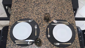 Mesa de granito rectangular con cuatro juegos de cubiertos y cristalería dispuestos para comer.
