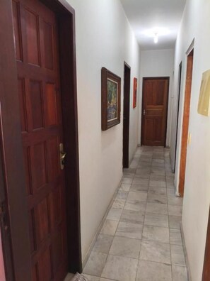 A hallway with a wooden door, tiled flooring, and framed pictures on the walls.