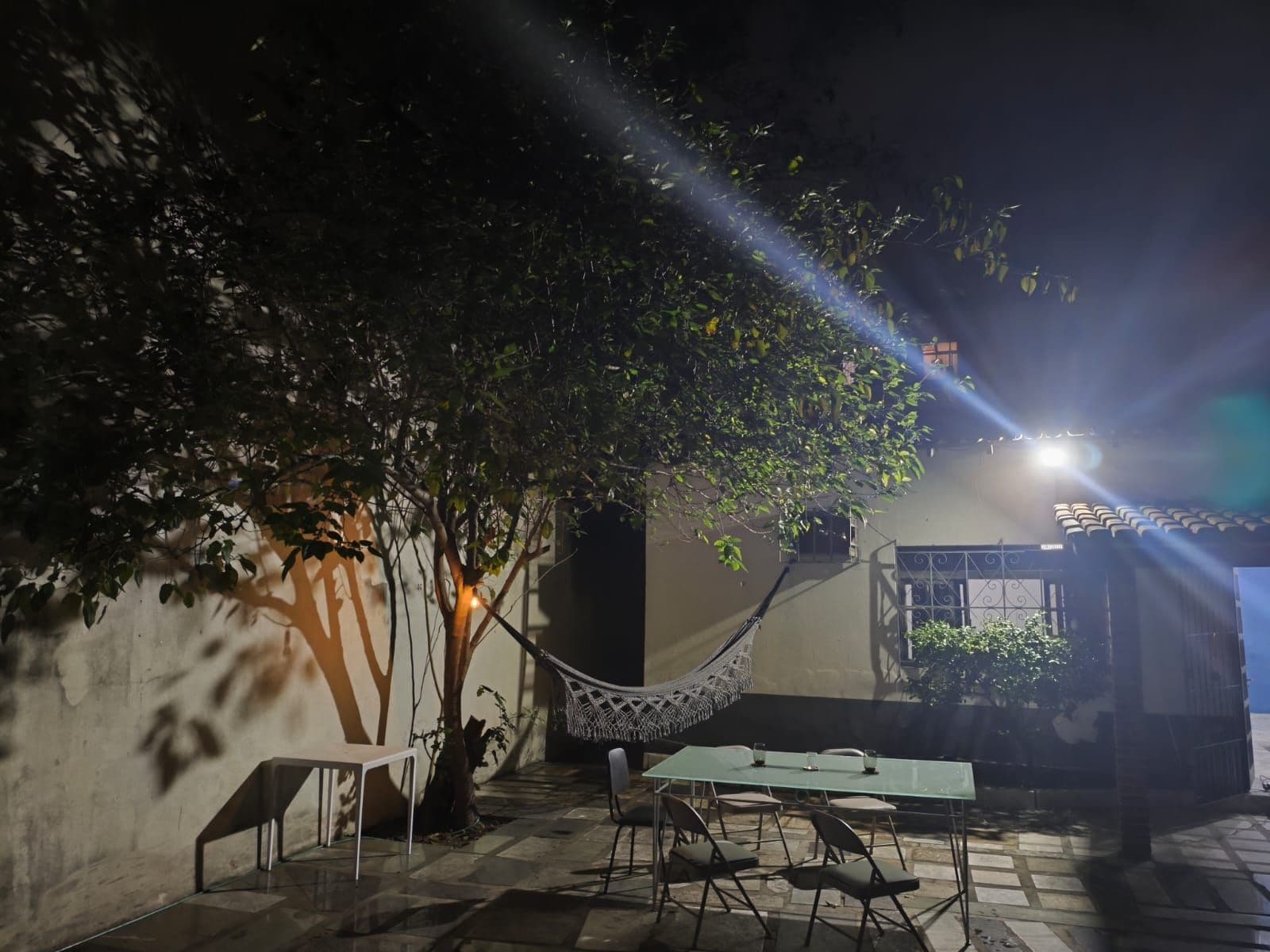 Un área de estar al aire libre con una mesa y sillas, una hamaca y un árbol que da sombra.