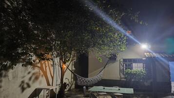 Un área de estar al aire libre con una mesa y sillas, una hamaca y un árbol que da sombra.