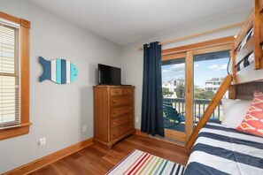 A bedroom with a bunk bed, a dresser, a television, and a view of a building through a window. - 8BR Ocean Views | Private Pool | Hot Tub | Beach (Nags Head)