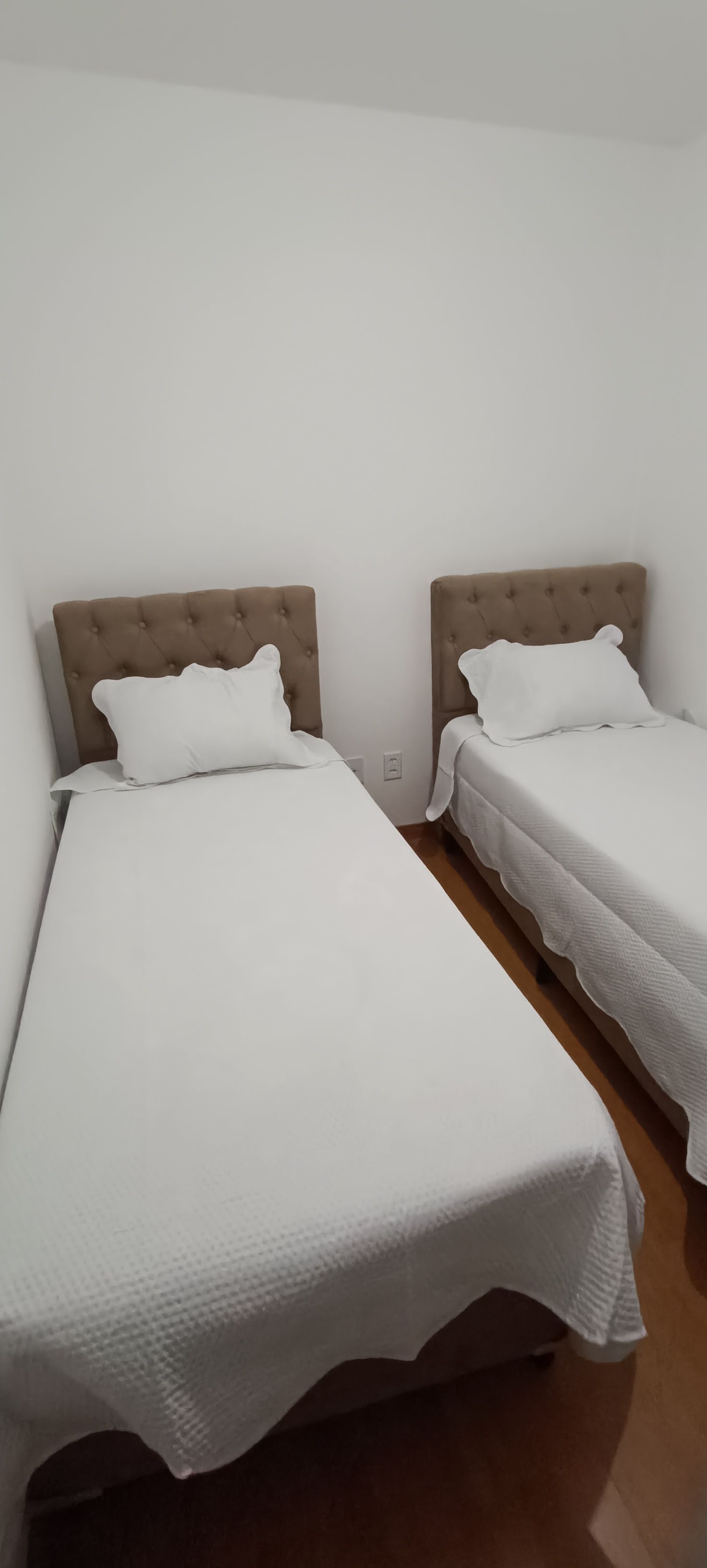 Zwei Einzelbetten mit Kopfteilen, weiße Bettwäsche und eine schlichte Wand.