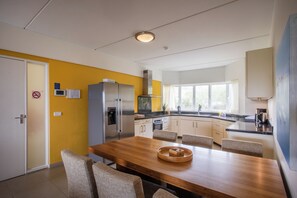 A modern kitchen with a dining area, featuring a stainless steel refrigerator, a microwave, and a wooden dining table with chairs. - Blue Bay Beachfront Apartment (Willemstad)
