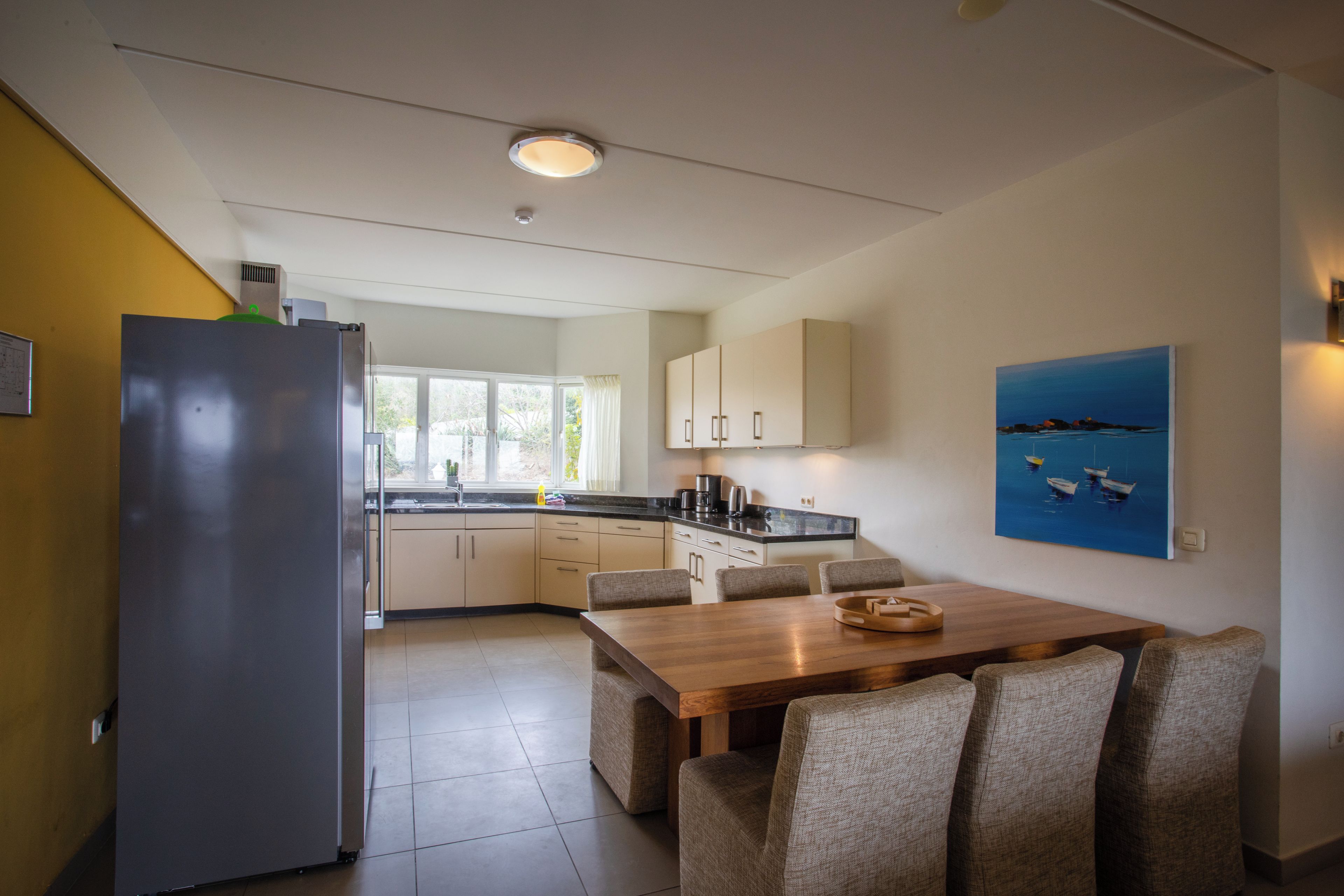 Una cocina moderna con comedor, que incluye un refrigerador, armarios y un cuadro con barcos en la pared.
