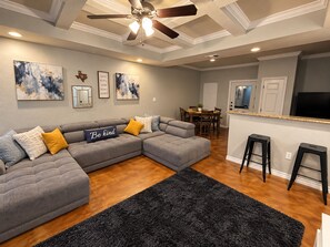 A modern living room with a sectional sofa, a black rug, and artwork on the walls. - Home Away from Home - 3/2 Townhome retreat 10 minutes from Randolph AFB (Selma)