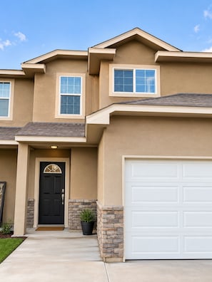 A two-story house with a black front door, a garage door, and a small front yard with a potted plant. - Home Away from Home - 3/2 Townhome retreat 10 minutes from Randolph AFB (Selma)