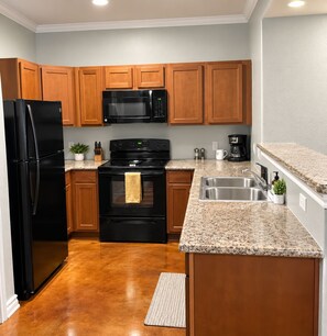 A kitchen with wooden cabinets, a black refrigerator, a microwave, a stove, and a granite countertop. - Home Away from Home - 3/2 Townhome retreat 10 minutes from Randolph AFB (Selma)
