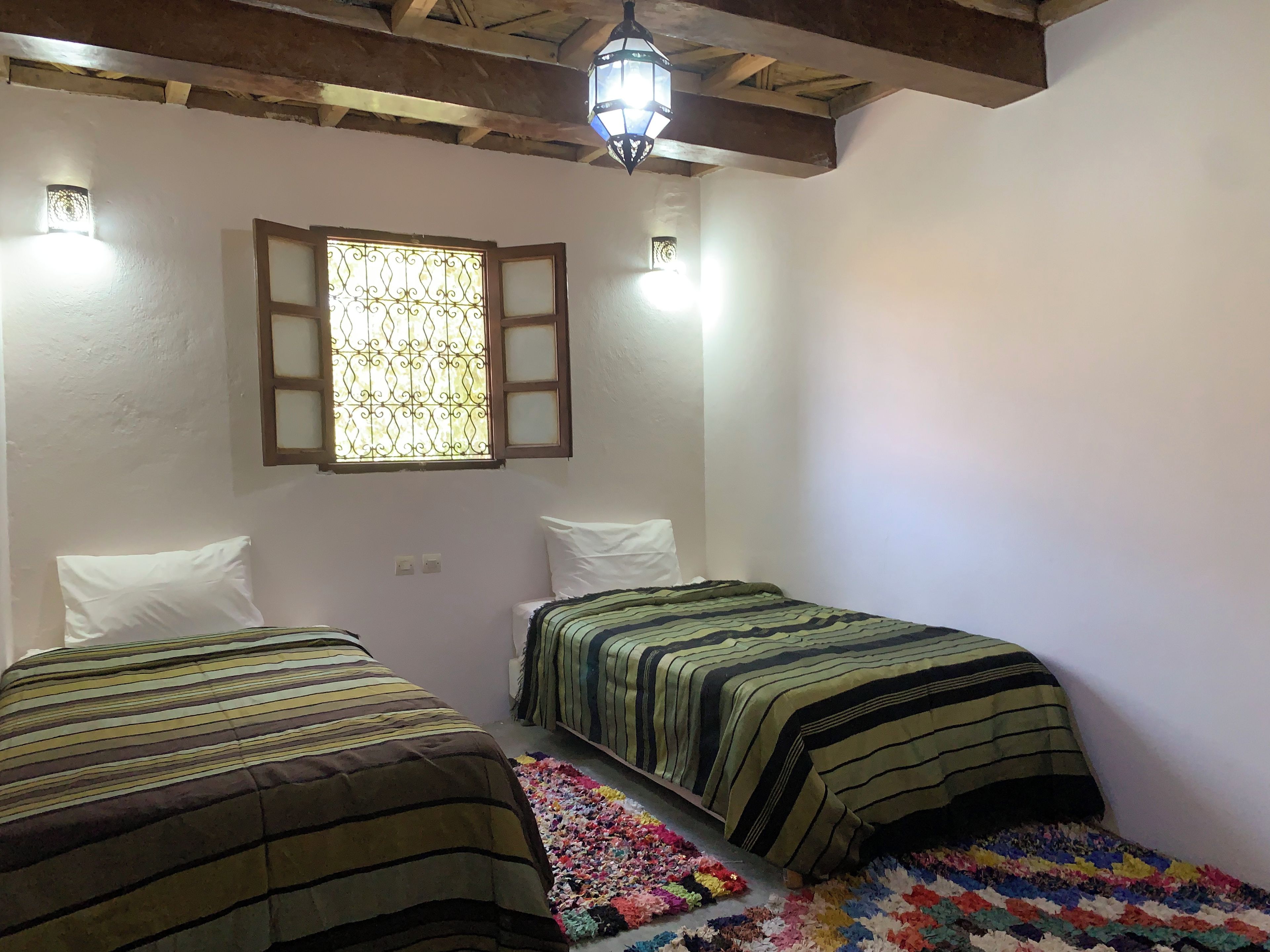 A room with two beds, a window with a decorative grille, and a hanging light fixture.