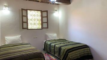A room with two beds, a window with a decorative grille, and a hanging light fixture.