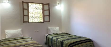 A room with two beds, a window with a decorative grille, and a hanging light fixture.