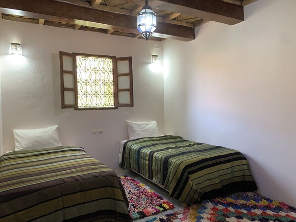 A room with two beds, a window with a decorative grille, and a hanging light fixture.