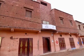 A building with multiple doors and windows, some with metal shutters, and a sign above the entrance.