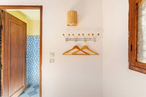 A hallway with a wooden door, a wall-mounted light fixture, a coat rack with two hangers, and a tiled wall.